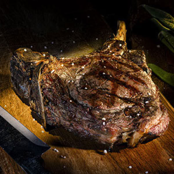 Gegrilltes Tomahowk-Steak auf einem Holzbrett mit grobem Salz bestreut.